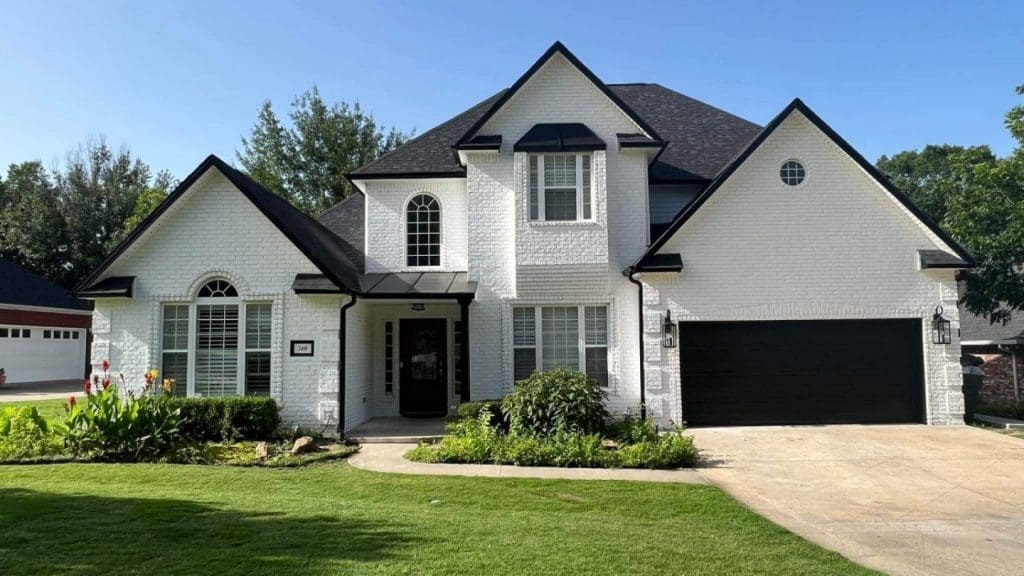 Exterior brick painting project by Derheim Painting — white painted brick with black trim and garage doors, Ardmore OK