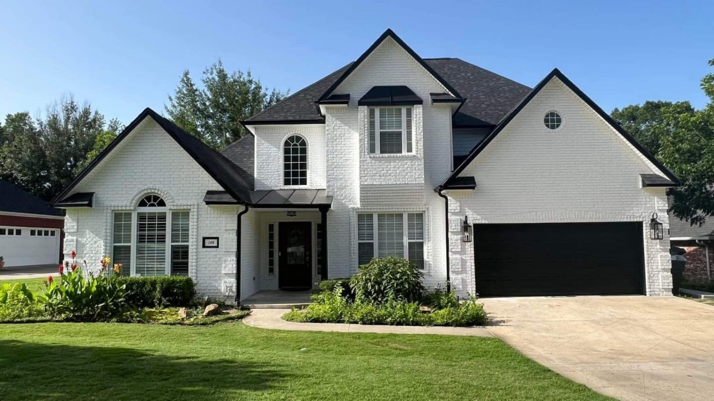Exterior brick painting project by Derheim Painting — white painted brick with black trim and garage doors, Ardmore OK