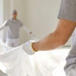 A professional painting crew wearing work gloves lays out a drop cloth before starting an interior painting project.